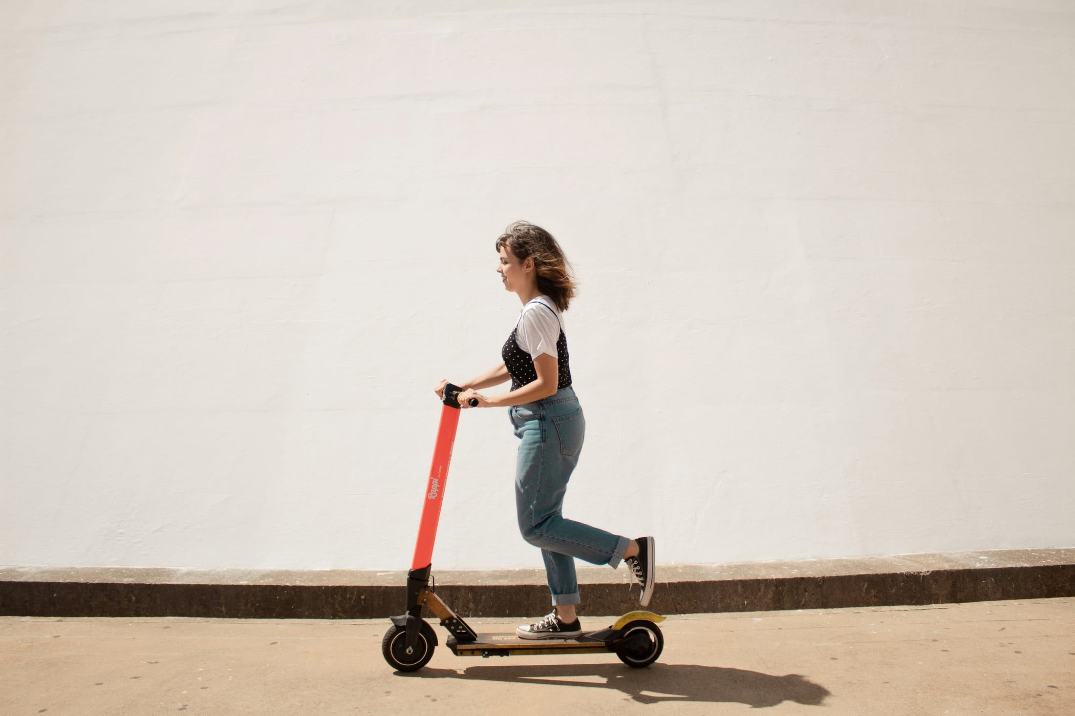 Personne roulant en trottinette électrique le long d’un mur clair